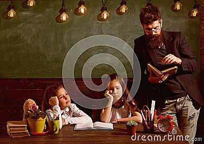 Boring lesson concept. Man with beard teaches schoolgirls, reading book. Bored and tired children listening teacher Stock Photo