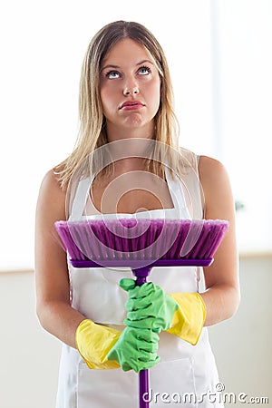 Boring young woman holding broom while cleaning at home. Stock Photo