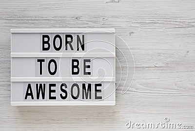 `Born to be awesome` words on a lightbox on a white wooden background, top view. Overhead, from above, flat lay. Copy space Stock Photo