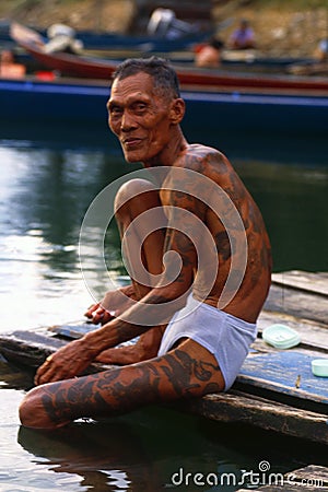 Borneo: Older Iban Headhunter with tatoo`s at the river sitting in the rain forest of Sarawak Editorial Stock Photo