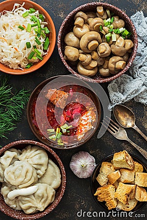 Borsch, dumplings, sauerkraut, pickled mushrooms. Russian dishes on a dark rustic background, top view. Traditional Russian cuisin Stock Photo