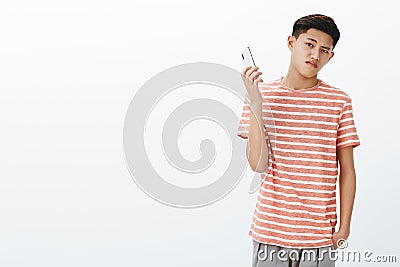 Bossy serious-looking cool young teenage asian guy in striped t-shirt taking away smartphone as being distracted. Guy Stock Photo