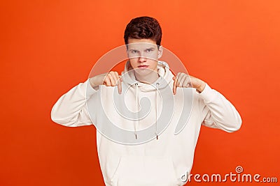 Bossy serious young man with stylish hirdo in casual hoodie pointing fingers down, demanding here and now, require Stock Photo