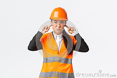 Bothered and displeased asian female chief engineer shut ears and grimacing from awful loud noise at construction area Stock Photo