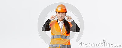 Bothered and displeased asian female chief engineer shut ears and grimacing from awful loud noise at construction area Stock Photo