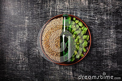 A bottle of beer on a green fresh hop and wheat grain in a plate against the background of a black scratched chalkboard Stock Photo