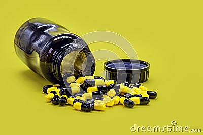 Bottle of black and yellow pills on yellow background, caseia aor caffeine pills used in bodybuilding for muscle mass Stock Photo