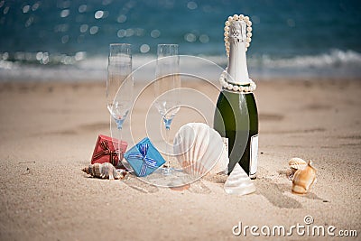 Bottle of champagne on the beach with a gift boxes and shells Stock Photo