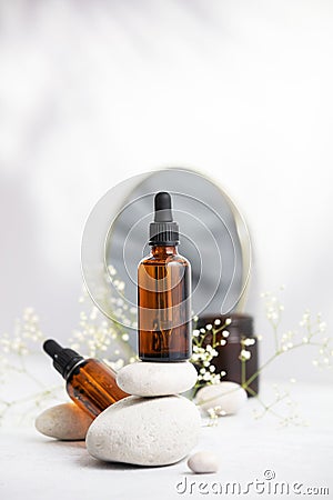 Bottle of dark amber glass with essential oil on stack of natural stones, candle and mirror Stock Photo