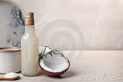 Bottle of delicious syrup, halves of coconut, flakes, cup of coffee and green leaves on white wooden table, space for text Stock Photo