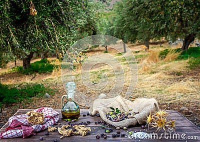 Bottle with extra virgin olive oil, olives, a fresh branch of olive tree and cretan rusk dakos close up on wooden table. Stock Photo