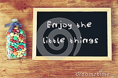 Bottle filled with candies and blackboard with the phrase enjoy the little things. Stock Photo