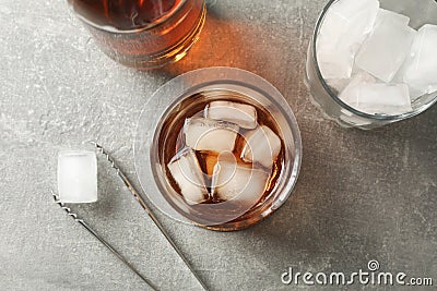 Bottle, glasses with ice cubes and whiskey on grey background Stock Photo