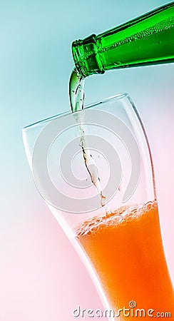 A bottle of green glass pouring beer into a beer glass. At an angle. Turquoise pink background. Close-up Stock Photo