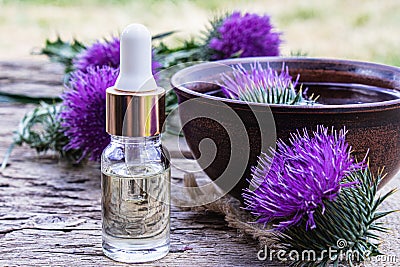 A bottle of tincture or potion`s essential oil and flowers of thistle on a wooden background Stock Photo