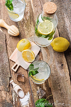 Bottle and two glasses of fresh lemonade with lemon slices, mint and ice on old wooden planks Stock Photo