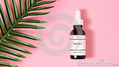 Bottle of a vitamin C serum resting on a pastel pink background next to a tropical green leaf Stock Photo