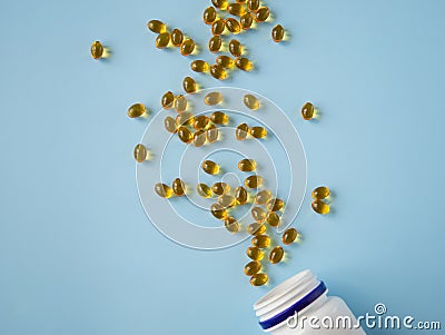 Bottle with vitamins capsules on a blue surface. Omega and vitamin D. Nutritional supplements. Opened bottle with yellow pills Stock Photo