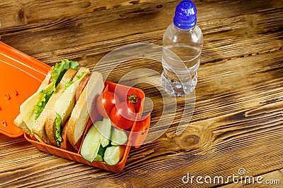 Bottle of water and lunch box with sandwiches and fresh vegetables on wooden table Stock Photo