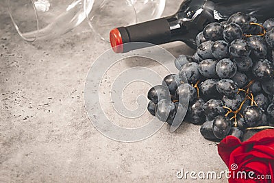 Bottle of wine, bunch of dark grapes, empty glass, rose on a gray background closeup Stock Photo