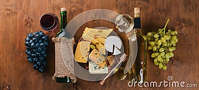 A bottle of wine, and a large assortment of cheeses, honey, nuts and spices, on a wooden table. Top view. Stock Photo