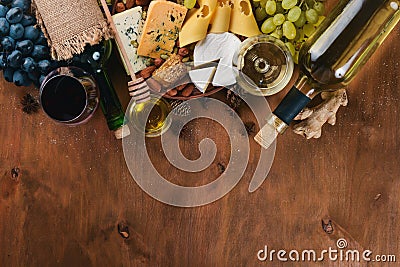 A bottle of wine, and a large assortment of cheeses, honey, nuts and spices, on a wooden table. Top view. Stock Photo