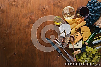 A bottle of wine, and a large assortment of cheeses, honey, nuts and spices, on a wooden table. Top view. Stock Photo