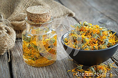 Bottles of calendula infusion, healthy marigold flowers in bowl and canvas sack on background. Herbal medicine Stock Photo