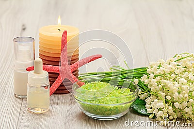 Bottles with cream for face skin and aromatic oil, bowl with sea salt, burning candle, starfish, hand massager and bouquet of Stock Photo