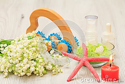 Bottles with cream for face skin and aromatic oil, bowl with sea salt, burning candle, starfish, hand massager and bouquet of Stock Photo