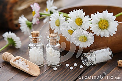 Bottles of homeopathy granules. Homeopathic remedy - Chamomilla. Daisies flowers in wooden bowl. Homeopathy medicine Stock Photo