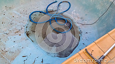 Bottom of drained swimming pool with just a little dirty water around the drain and a vacuum hose curled nearby with section of Stock Photo