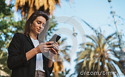 Bottom view-a cute businesswoman typing on a smartphone while standing in middle of a Park in city of Barcelona on summer day Stock Photo