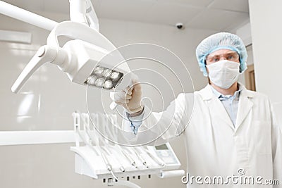 Bottom view of a doctor portrait dentist, surgeon in uniform and mask on his face, wearing glasses, holding lamp in her Stock Photo