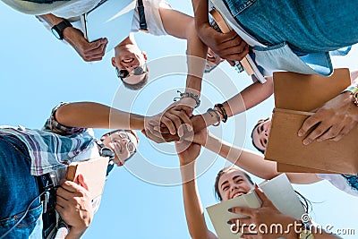 bottom view of smiling multiethnic teenage classmates stacking hands in park Stock Photo