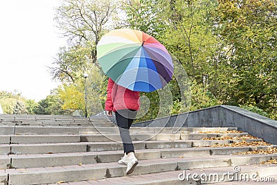 Bottom view of young female with big multicolored umbrella coming outdoor upstairs Stock Photo