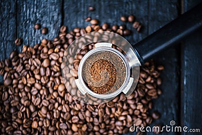 Bottomless filter with grind beans on a wooden black table. Roasted coffee beans. Espresso coffee extraction. Prepare of espresso. Stock Photo