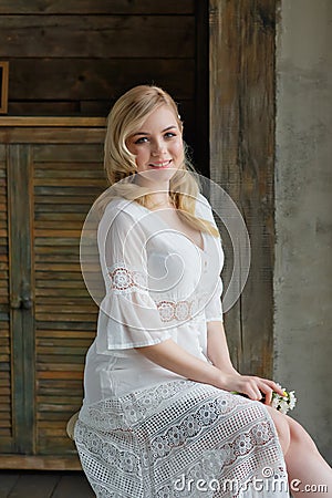 Boudoir photo of the bride in the morning. A beautiful portrait of a young blonde woman in a white coat sitting by the window Stock Photo