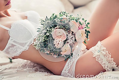 Boudoir wedding morning. Beautiful sexy bride in white underwear with garter belt and bouquet in soft defocus Stock Photo