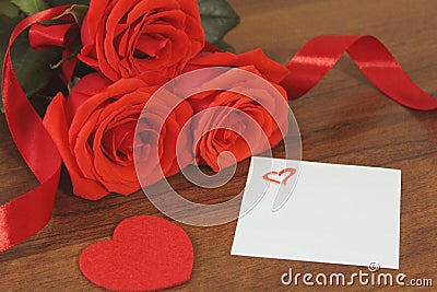 Bouguet of red roses tied with red satin ribbon, a souvenir in the for of heart of red color and a small piece of paper painted h. Stock Photo