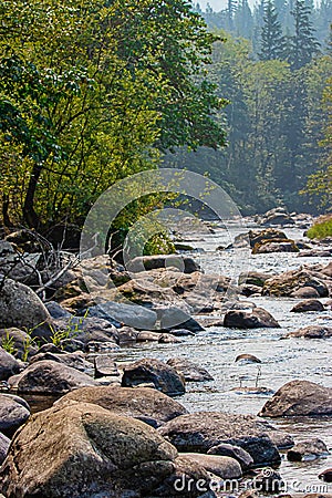 Boulders and large rocks rise out of wide flat river in summer Stock Photo