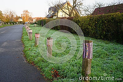 Boundary roadside poles decorated with knitted products against the background of grass with hoarfrost in November. Berlin Stock Photo