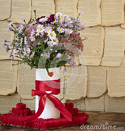 A bouquet of beautiful autumn flowers in a white vase with a red ribbon. Behind the pages of books. Colourfull Stock Photo