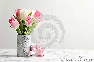 Bouquet of beautiful spring tulips in vase and gift box on marble table against light background. Stock Photo