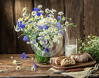 Bouquet of field flowers, glass of milk and soft bread. Stock Photo