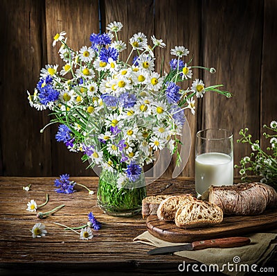 Bouquet of field flowers, glass of milk and soft bread. Stock Photo