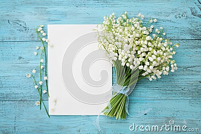 Bouquet of flowers lily of the valley and empty paper sheet on turquoise rustic table from above, beautiful vintage card, top view Stock Photo