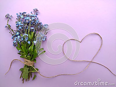 A bouquet of forget me nots tied with a rope of jute on a lilac background Stock Photo