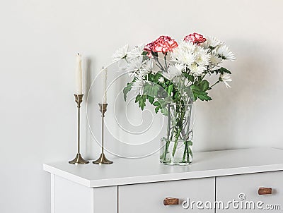 A bouquet of fresh chrysanthemums and carnations, candles in brass candlesticks on a white cabinet in the living room Stock Photo