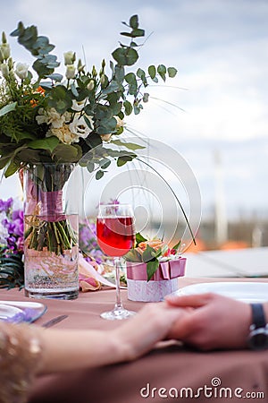 A bouquet in a glass vase, a glass of wine, a small gift, the intertwined hands of a man and a woman Stock Photo